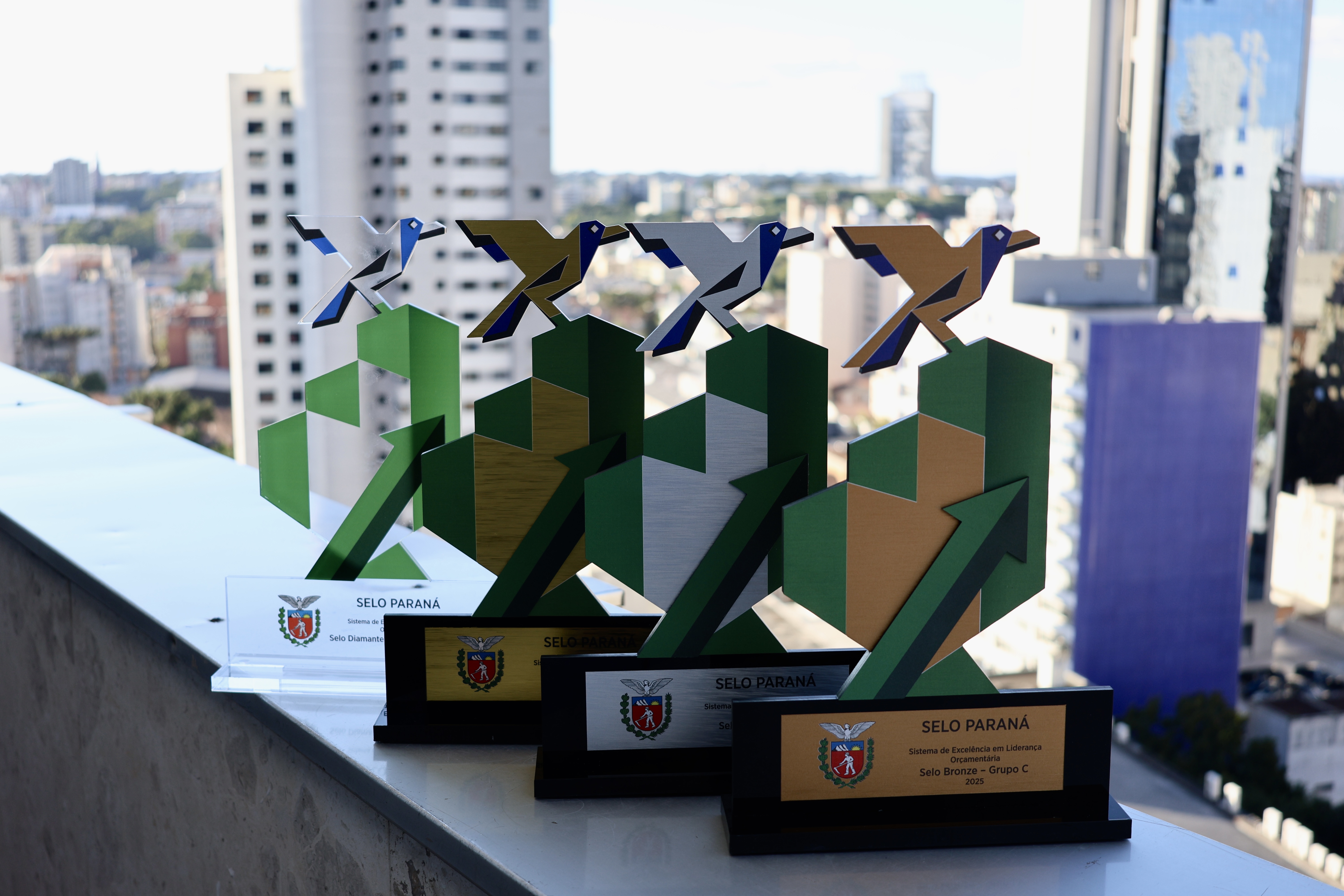 Quatro troféus Selo Paraná com uma paisagem urbana ao fundo.