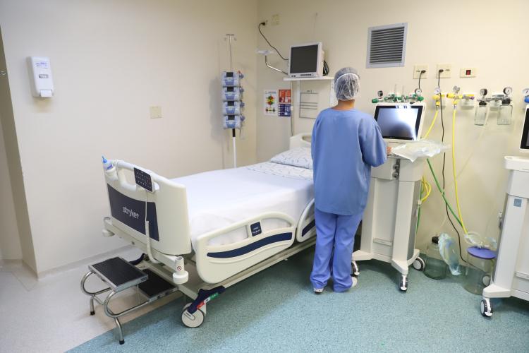 Leito de hospital com enfermeira de costas mexendo nos aparelhos