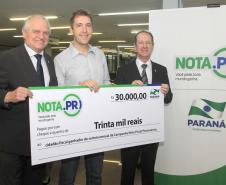 O psicólogo curitibano Marcio Simioni recebeu nesta quarta-feira (18) um cheque simbólico do primeiro prêmio mensal da campanha Nota Fiscal Paranaense, no valor de R$ 30 mil. Ele foi contemplado no sorteio realizado no dia 28 de maio. Outra premiada foi a professora Rosane Bihre Mattes, da rede municipal de ensino de Curitiba, que recebeu um cheque simbólico de R$ 20 mil, referente a um prêmio semanal acumulado.